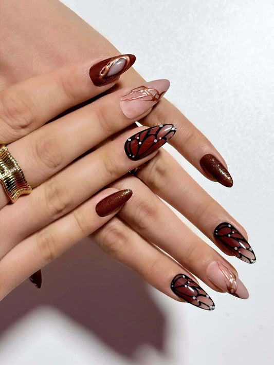 Butterfly wing press on nails in warm brown and nude pink tones, with delicate line art details. Perfect for daily use, office and holidays. Medium length almond shape fake nails with an elegant, artistic finish.
